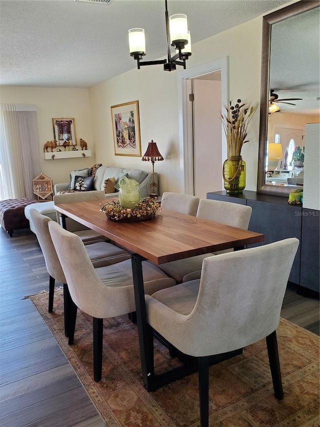 dining space with ceiling fan with notable chandelier, a textured ceiling, and dark wood-type flooring