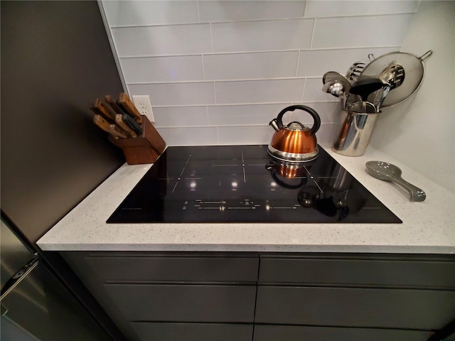 interior details featuring light stone counters, black electric cooktop, and backsplash