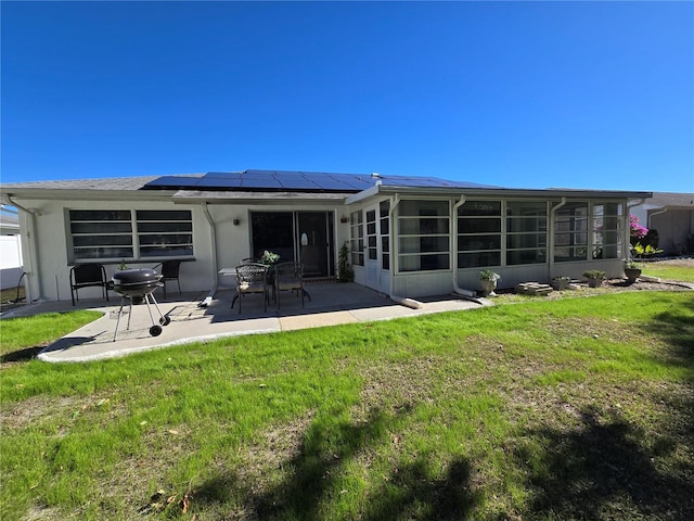 rear view of property featuring a lawn, a sunroom, a patio, and solar panels