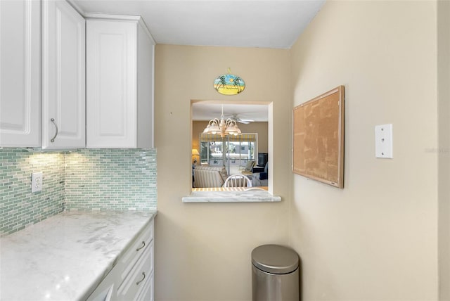 kitchen with decorative backsplash, white cabinets, light stone countertops, and ceiling fan with notable chandelier