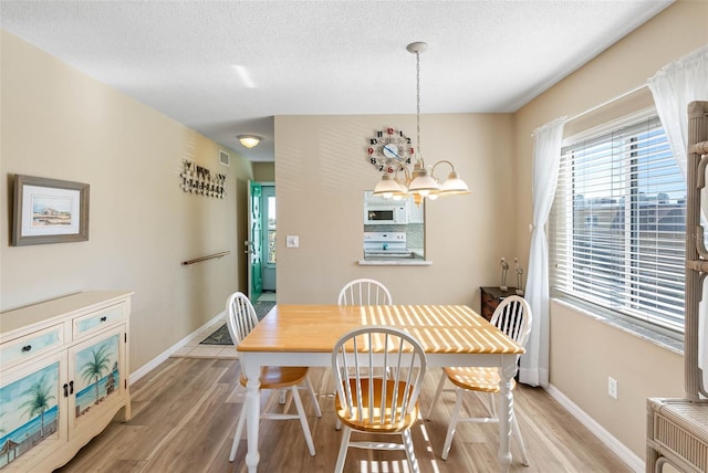 dining area with a notable chandelier, light wood-type flooring, and a textured ceiling