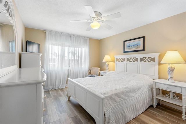 bedroom with a textured ceiling, light hardwood / wood-style flooring, and ceiling fan