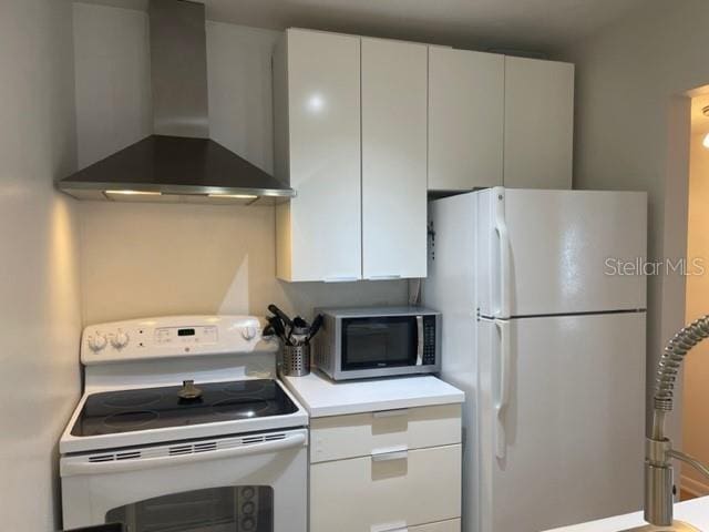 kitchen with white cabinets, white appliances, and wall chimney range hood