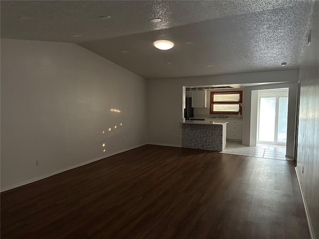 unfurnished living room with light hardwood / wood-style floors, a textured ceiling, and vaulted ceiling