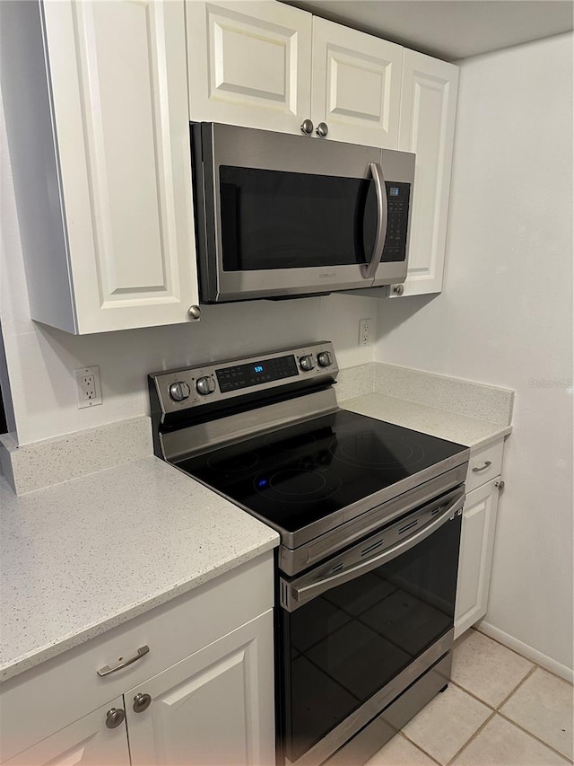 kitchen with white cabinets, appliances with stainless steel finishes, light tile patterned floors, and light stone countertops