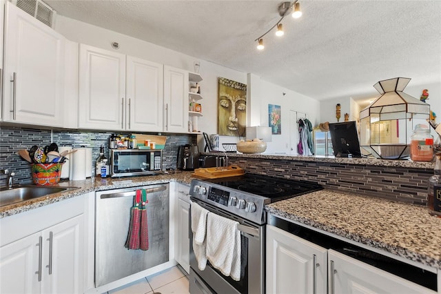 kitchen with appliances with stainless steel finishes, a textured ceiling, white cabinetry, and backsplash