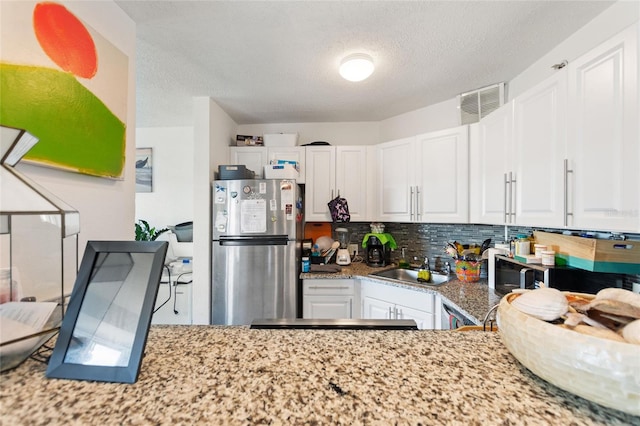 kitchen featuring stainless steel fridge, white cabinets, and a textured ceiling