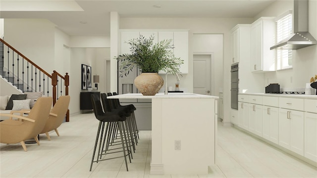 kitchen with white cabinets, a breakfast bar, a kitchen island, and wall chimney exhaust hood