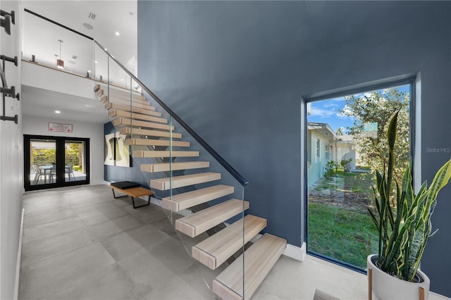 stairway with concrete flooring, a towering ceiling, and french doors