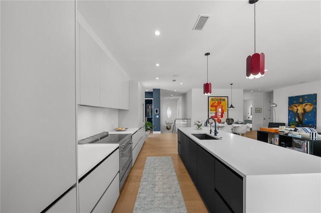 kitchen featuring white cabinetry, a large island, high end stove, pendant lighting, and sink