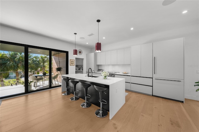 kitchen featuring pendant lighting, a kitchen bar, white cabinetry, light wood-type flooring, and an island with sink