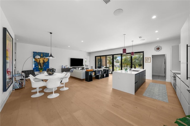 kitchen featuring hanging light fixtures, sink, an island with sink, and light hardwood / wood-style floors