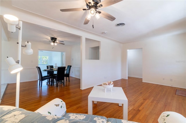 living room featuring wood-type flooring, ceiling fan, and ornamental molding