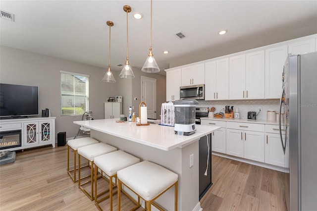 kitchen with light hardwood / wood-style floors, decorative light fixtures, decorative backsplash, a center island with sink, and appliances with stainless steel finishes