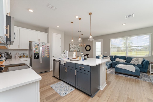 kitchen featuring pendant lighting, a center island with sink, light hardwood / wood-style floors, white cabinetry, and stainless steel appliances