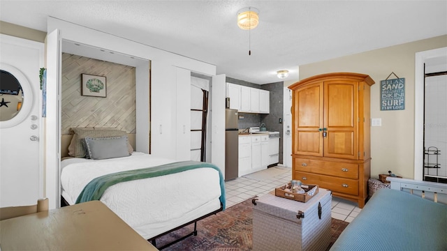 bedroom featuring stainless steel fridge, light tile patterned floors, ensuite bathroom, and a textured ceiling