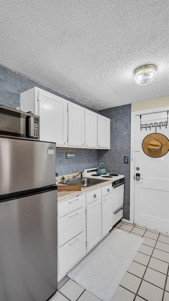 kitchen with a textured ceiling, white cabinetry, white electric range, and stainless steel refrigerator