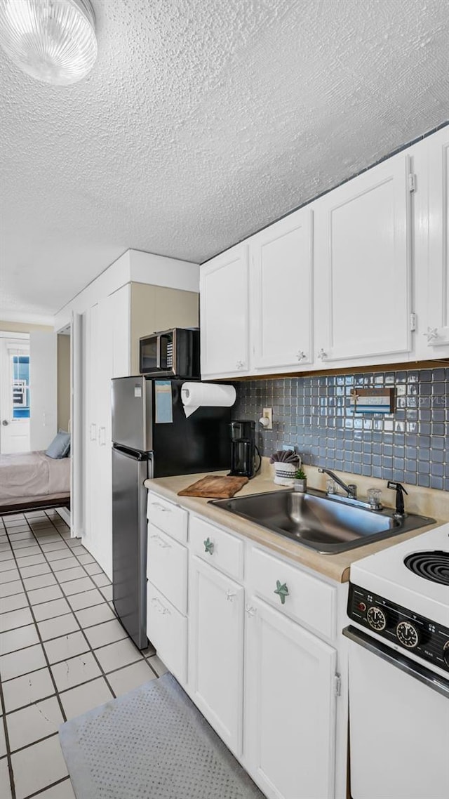 kitchen featuring tasteful backsplash, stainless steel appliances, sink, light tile patterned floors, and white cabinets