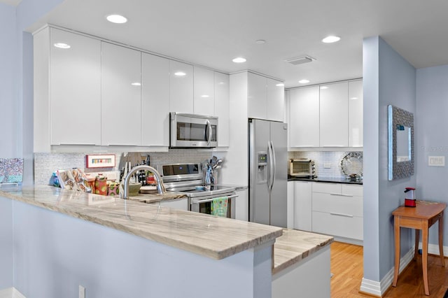 kitchen featuring kitchen peninsula, appliances with stainless steel finishes, light stone countertops, light hardwood / wood-style flooring, and white cabinets