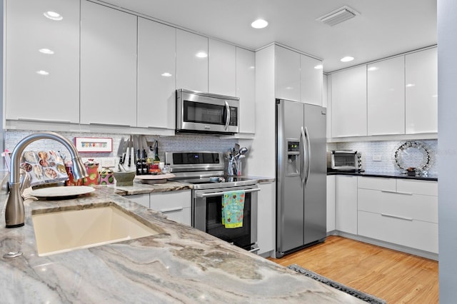 kitchen with light stone counters, sink, white cabinets, and appliances with stainless steel finishes