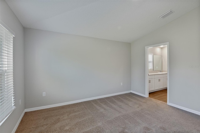 unfurnished bedroom with sink, light colored carpet, lofted ceiling, and ensuite bathroom