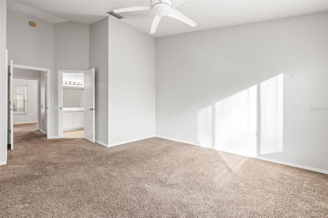 carpeted empty room featuring ceiling fan and a towering ceiling