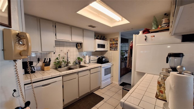 kitchen with tile countertops, white appliances, backsplash, light tile patterned floors, and sink