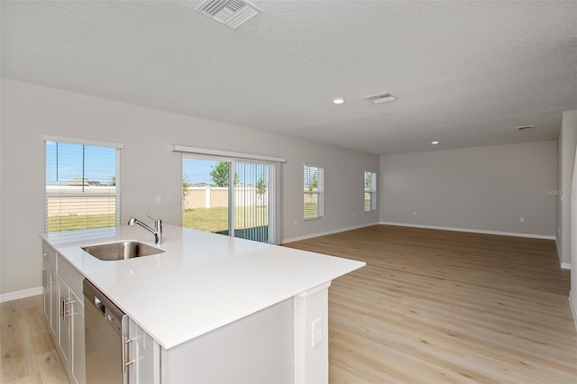 kitchen with dishwasher, sink, an island with sink, light hardwood / wood-style floors, and a textured ceiling