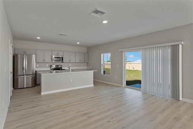 kitchen featuring appliances with stainless steel finishes, light wood-type flooring, gray cabinetry, a kitchen island with sink, and sink