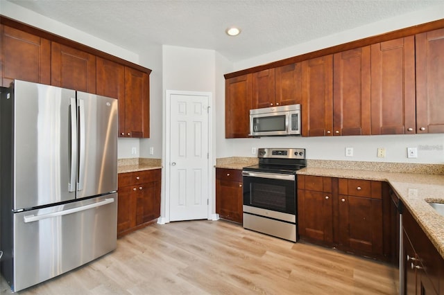 kitchen featuring light stone counters, stainless steel appliances, a textured ceiling, and light wood-type flooring