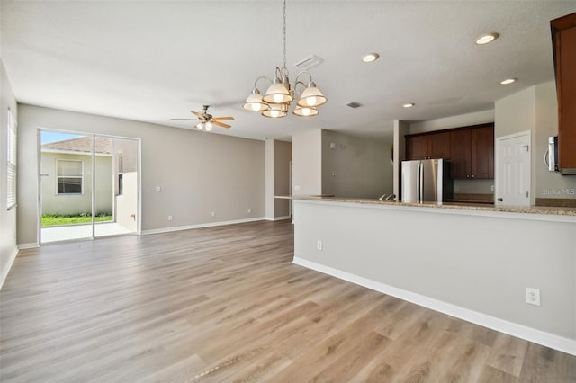 unfurnished living room with ceiling fan with notable chandelier and light hardwood / wood-style flooring