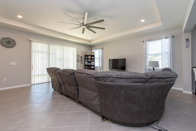 tiled living room with ceiling fan and a raised ceiling