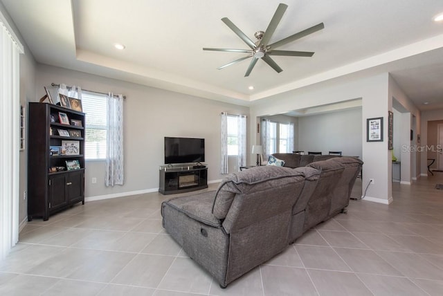 tiled living room featuring a raised ceiling, plenty of natural light, and ceiling fan