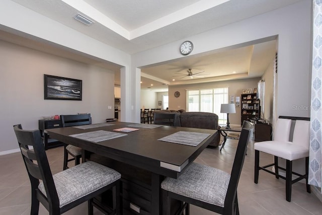 tiled dining space with a tray ceiling and ceiling fan