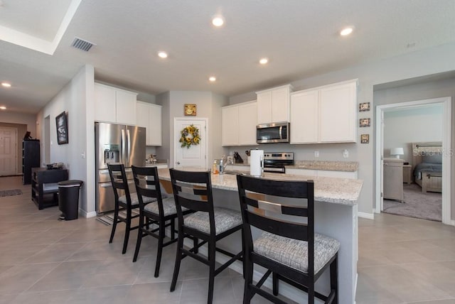 kitchen featuring a center island with sink, a breakfast bar, white cabinets, and stainless steel appliances