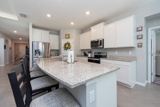 kitchen with white cabinets, sink, an island with sink, appliances with stainless steel finishes, and light stone counters