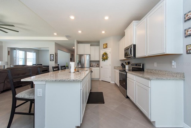 kitchen with light stone countertops, a center island with sink, white cabinets, and appliances with stainless steel finishes