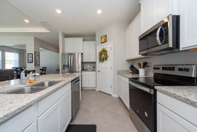 kitchen with white cabinets, appliances with stainless steel finishes, light stone countertops, and sink