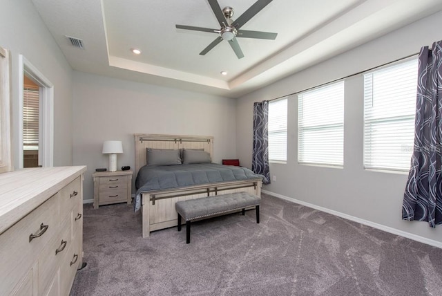 bedroom with a raised ceiling, ceiling fan, and dark colored carpet