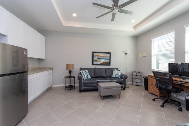 tiled office space with a raised ceiling and ceiling fan