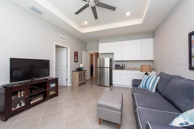 tiled living room with a tray ceiling and ceiling fan