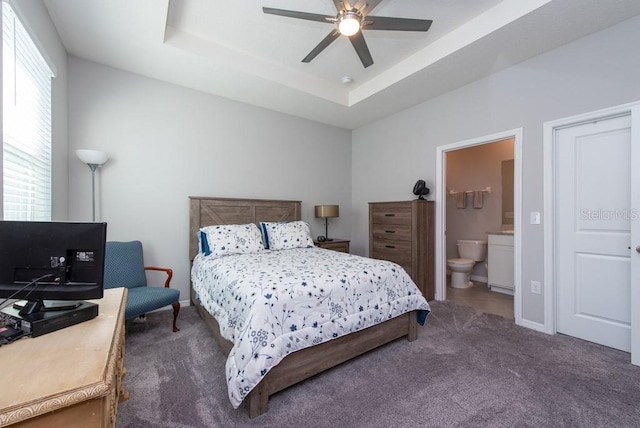 carpeted bedroom featuring a tray ceiling, ensuite bathroom, and ceiling fan