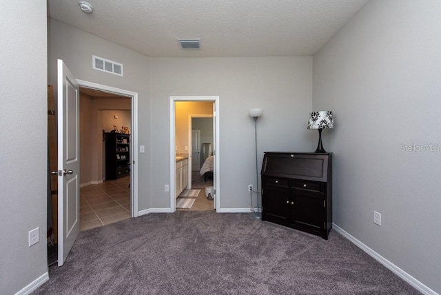 unfurnished bedroom featuring carpet flooring, ensuite bath, and a textured ceiling