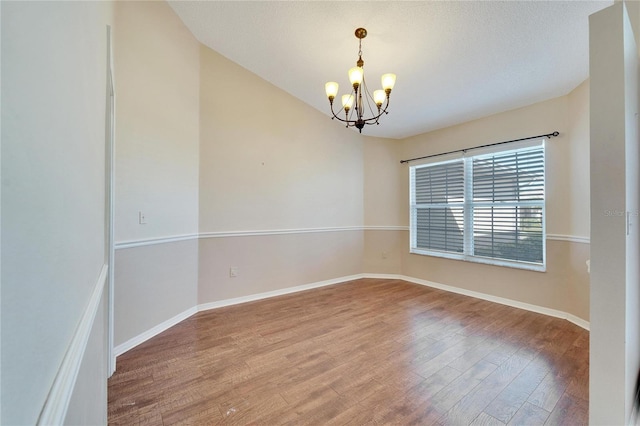 spare room featuring hardwood / wood-style floors, a textured ceiling, and an inviting chandelier