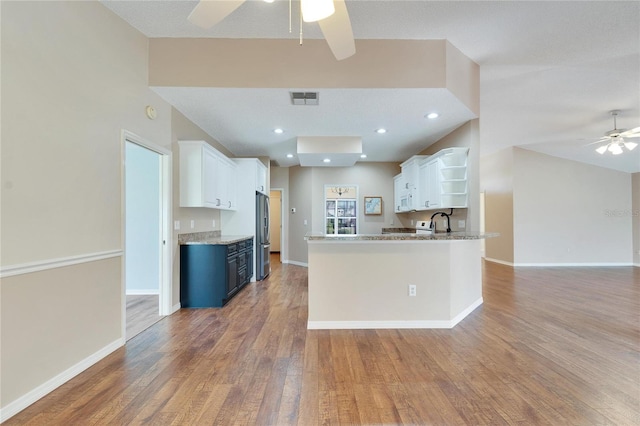 kitchen with white cabinets, kitchen peninsula, hardwood / wood-style floors, and stainless steel refrigerator