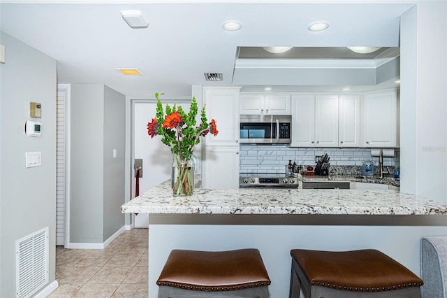 kitchen featuring kitchen peninsula, a kitchen breakfast bar, backsplash, stainless steel appliances, and white cabinets