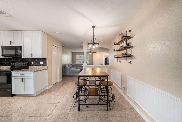 kitchen featuring decorative backsplash, white cabinets, black appliances, and decorative light fixtures