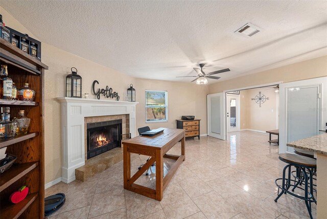 living room featuring light tile patterned floors, a textured ceiling, ceiling fan, and a tiled fireplace