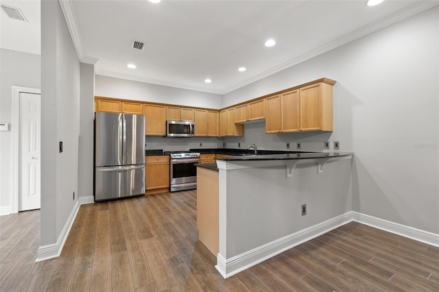 kitchen with kitchen peninsula, hardwood / wood-style floors, appliances with stainless steel finishes, ornamental molding, and sink