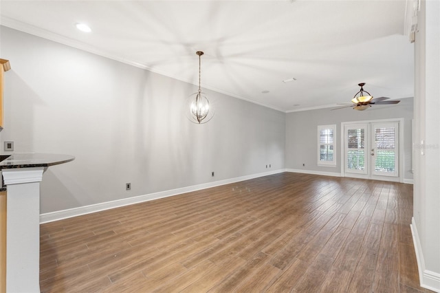 unfurnished living room featuring ceiling fan with notable chandelier, hardwood / wood-style flooring, and crown molding